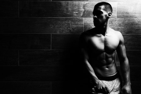 Healthy Young Man Standing Strong Standing Against a Wall and Flexing Muscles - Muscular Athletic Bodybuilder Fitness Model Posing After Exercises - a Place for Your Textの写真素材