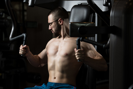 Handsome Muscular Fitness Man Wearing Glasses Doing Heavy Weight Exercise For Chest On Machine With Cable In The Gymの写真素材