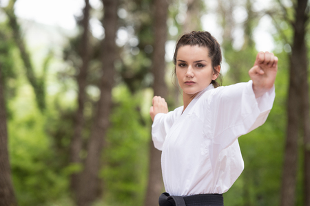 Young Woman Practicing Her Karate Moves in Wooded Forest Area - White Kimono - Black Beltの写真素材