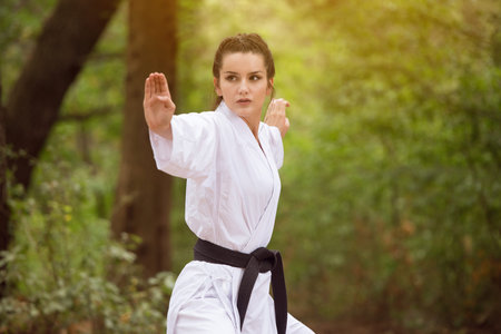 Young Woman Dressed In Traditional Kimono Practicing Her Karate Moves in Wooded Forest Area - Black...