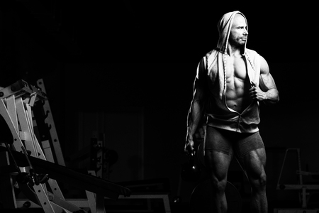 Man Working Out With Kettle Bell In A Dark Gym - Bodybuilder Doing Heavy Weight Exercise With Kettle-bellの写真素材