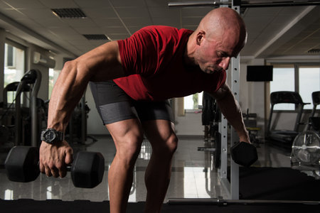 Serious Bodybuilder Doing Heavy Weight Exercise For Trapezius or Back With Dumbbells