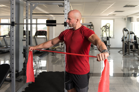 Attractive Man Exercising With A Resistance Band In Gym As Part Of Fitness Bodybuilding Trainingの写真素材