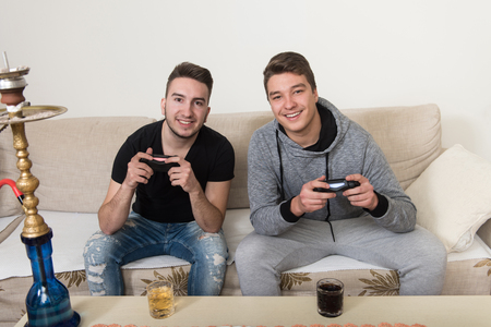 Two Brothers or Friends Playing Video Games Together as They Relax on a Couch in the Living Roomの写真素材
