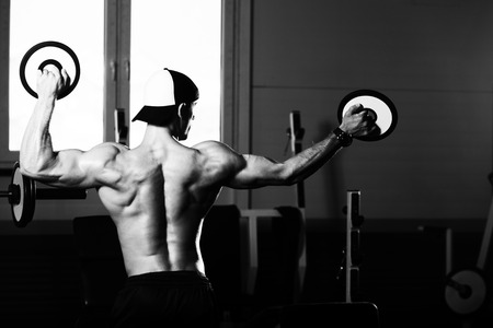Healthy Young Man Standing Strong In The Gym And Flexing Muscles With Weights - Muscular Athletic Bodybuilder Fitness Model Posing After Exercisesの写真素材