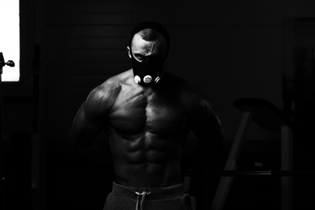 Healthy Young Man Standing Strong  In Elevation Mask And Flexing Muscles - Muscular Athletic Bodybuilder Fitness Model Posing After Exercisesの写真素材