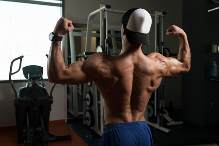 Healthy Young Man Standing Strong In The Gym And Flexing Muscles - Muscular Athletic Bodybuilder Fitness Model Posing After Exercisesの写真素材
