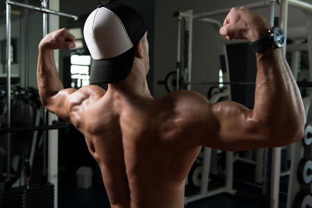 Healthy Young Man Standing Strong In The Gym And Flexing Muscles - Muscular Athletic Bodybuilder Fitness Model Posing After Exercisesの写真素材