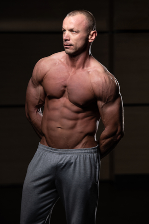 Young Man Standing Strong In The Gym And Flexing Muscles - Muscular Athletic Bodybuilder Fitness Model Posing After Exercisesの写真素材