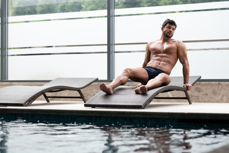 Young Man Resting On Sun Loungers By Swimming Pool And Flexing Muscles