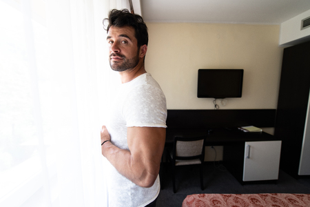 Young Man Standing at Window in Confident Pose Looking at Cityの写真素材