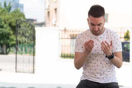 Muslim Man Making Traditional Prayer to God Allah Outdoors at Front the Mosque