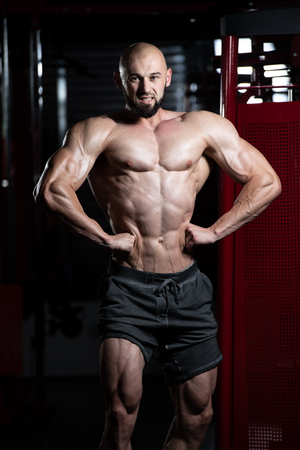 Young Man Standing Strong In The Gym And Flexing Muscles - Muscular Athletic Bodybuilder Fitness Model Posing After Exercisesの写真素材