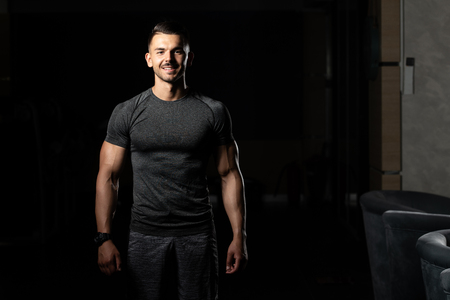 Young Man Standing Strong In The Gym And Flexing Muscles - Muscular Athletic Bodybuilder Fitness Model Posing After Exercisesの写真素材