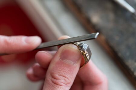 Hardworking Goldsmith Working On An Unfinished Gold Ring With His Hands And Toolsの写真素材