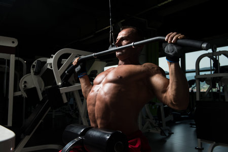 Handsome Bodybuilder Doing Heavy Weight Exercise For Back On Machine