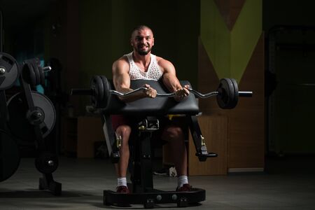 Muscular Man Doing Heavy Weight Exercise For Biceps With Barbell In Gymの写真素材