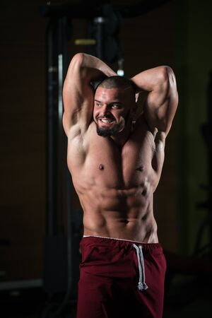 Healthy Young Man Standing Strong In The Gym And Flexing Muscles - Muscular Athletic Bodybuilder Fitness Model Posing After Exercisesの写真素材