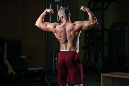 Healthy Young Man Standing Strong In The Gym And Flexing Muscles - Muscular Athletic Bodybuilder...