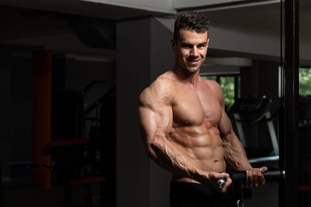Muscular Fitness Bodybuilder Doing Heavy Weight Exercise For Biceps On Machine With Cable In The Gym