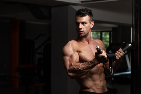Muscular Fitness Bodybuilder Doing Heavy Weight Exercise For Biceps On Machine With Cable In The Gym