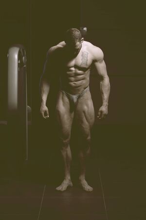 Handsome Young Man Standing Strong In The Gym And Flexing Muscles - Muscular Athletic Bodybuilder Fitness Model Posing After Exercisesの写真素材