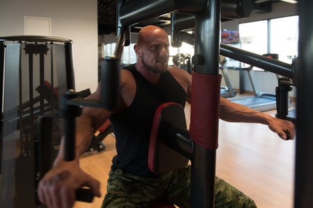 Muscular Fitness Bodybuilder Doing Heavy Weight Exercise For Shoulders On Machine With Cable In The...