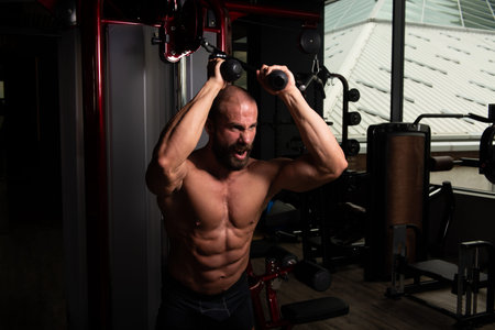 Muscular Fitness Bodybuilder Doing Heavy Weight Exercise For Triceps On Machine With Cable In The...