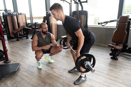 Personal Trainer Showing Young Man How to Train Back With Barbell in the Gymの写真素材