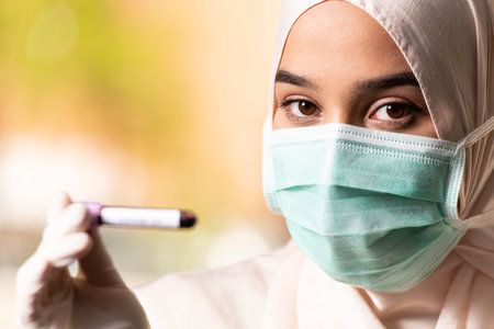 Muslim Woman Doctor With Surgical Mask and Gloves Holding a Blood Test Tube Which is Signed as...