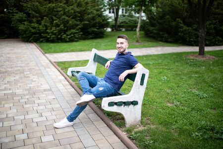 Portrait of a Confident and Successful Young Man With Blue Shirt Outside in Park Sitting on Benchの写真素材