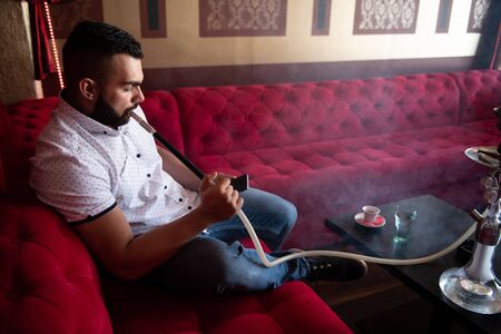 Man Smoking Turkish Hookah In The Cafe With Colorful Walls On Background and Texting on Phoneの写真素材