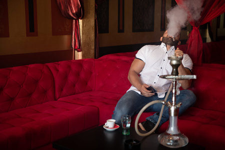 Young Man Smoking Shisha At Arabic Restaurant - Man Exhaling Smoke Inhaling From A Hookah and...
