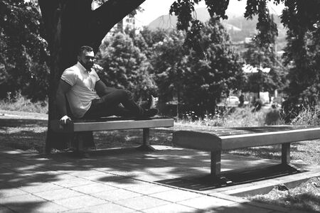 Portrait of a Confident and Successful Young Man With White Shirt Outside in Park Sitting on Benchの写真素材