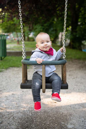 Happy Laughing Toddler Boy Having Fun on a Swing Enjoying a Day on a Playground in a Parkの写真素材