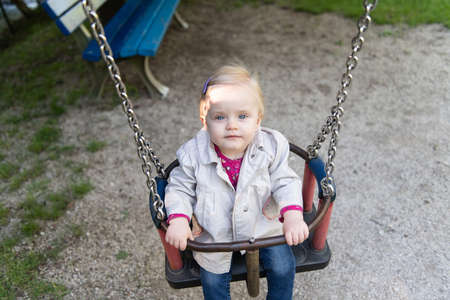 Happy Laughing Toddler Girl Having Fun on a Swing Enjoying a Day on a Playground in a Parkの写真素材