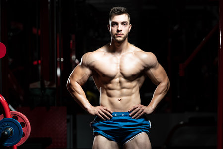 Young Man Standing Strong In The Gym And Flexing Muscles - Muscular Athletic Bodybuilder Fitness...