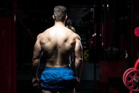 Young Man Standing Strong In The Gym And Flexing Muscles - Muscular Athletic Bodybuilder Fitness Model Posing After Exercisesの写真素材
