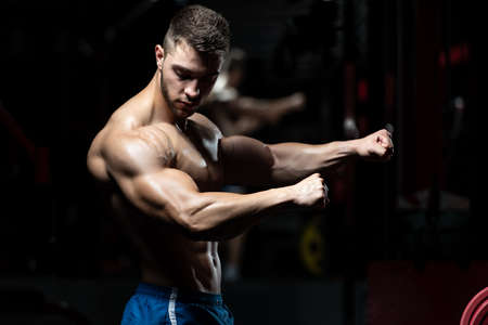 Young Man Standing Strong In The Gym And Flexing Muscles - Muscular Athletic Bodybuilder Fitness Model Posing After Exercisesの写真素材