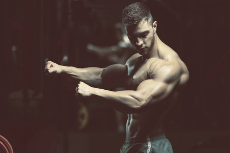 Young Man Standing Strong In The Gym And Flexing Muscles - Muscular Athletic Bodybuilder Fitness...