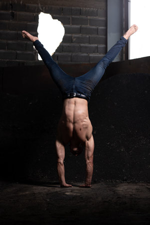 Handsome Man Keeping Balance on Hands in Warehouse - Muscular Athletic Bodybuilder Fitness Model...