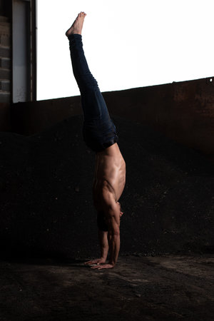 Handsome Man Keeping Balance on Hands in Warehouse - Muscular Athletic Bodybuilder Fitness Model...