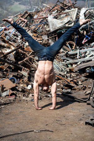 Handsome Man Keeping Balance on Hands in Old Industrial Junk Yard - Muscular Athletic Bodybuilder Fitness Model Doing Handstand Push-upの写真素材