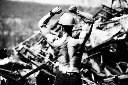 Handsome Man Standing Strong in Scrap Metal Industrial Junkyard and Flexing Muscles - Muscular...