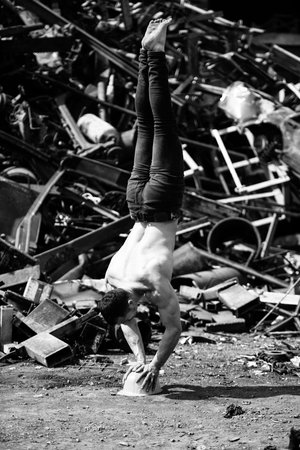 Handsome Man Keeping Balance on on Yellow Helmet With Hands in Old Industrial Junk Yard - Muscular...