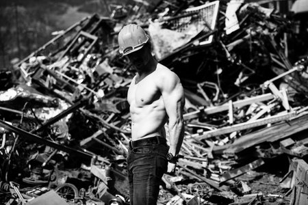 Young Man Standing Strong in Old Scrap Metal Garage and Flexing Muscles - Muscular Athletic...