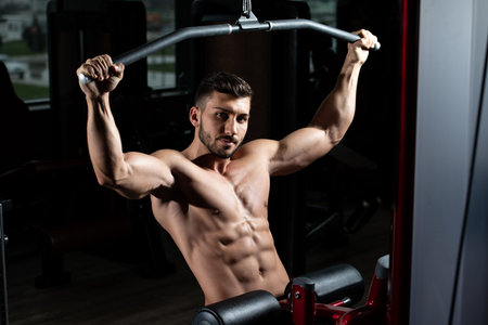Handsome Bodybuilder Doing Heavy Weight Exercise For Back On Machine