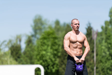 Man Exercising With Kettle Bell Outdoor and Flexing Muscles - Muscular Athletic Bodybuilder Fitness Model Exercisesの写真素材