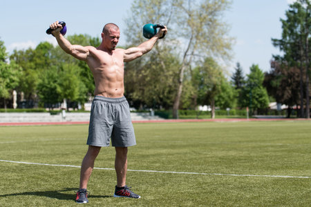 Man Exercising With Kettle Bell Outdoor and Flexing Muscles - Muscular Athletic Bodybuilder Fitness Model Exercisesの写真素材