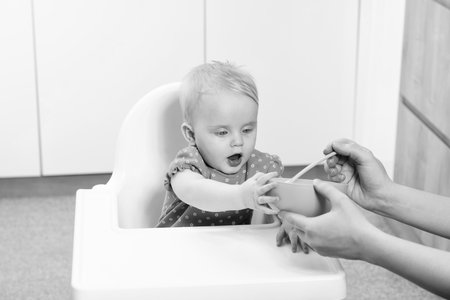 Mother Feeding Her Baby Daughter With Spoon - Mother Giving Healthy Food To Her Adorable Child At Homeの写真素材